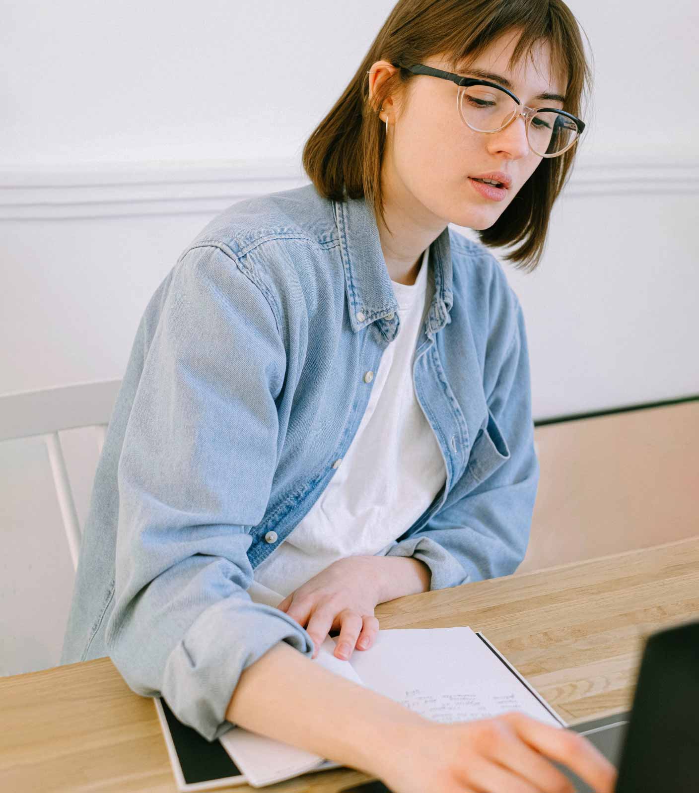 A female student with glasses sitting at a desk with a sheet of paper and a computer photographed from the front.
