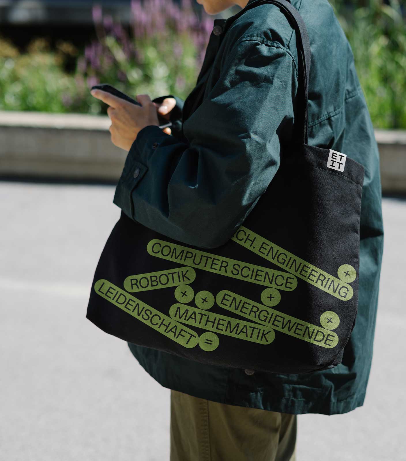A student wearing a green jacket and olive pants with a black tote bag on their shoulder with multiple neon green-yellow bubbles with ETIT topics in them.