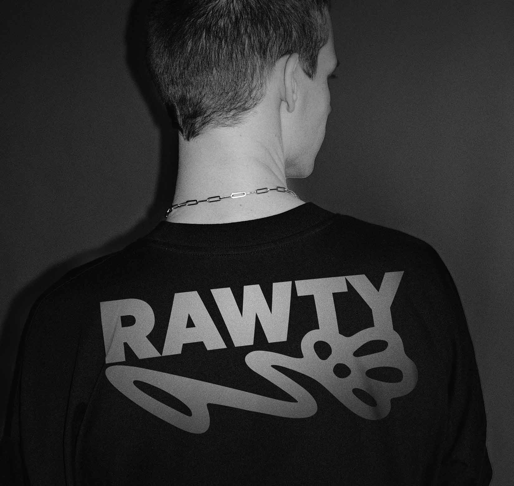 A black and white photo of person standing with the back to the camera wearing a black t-shirt with the white RAWTY logo.