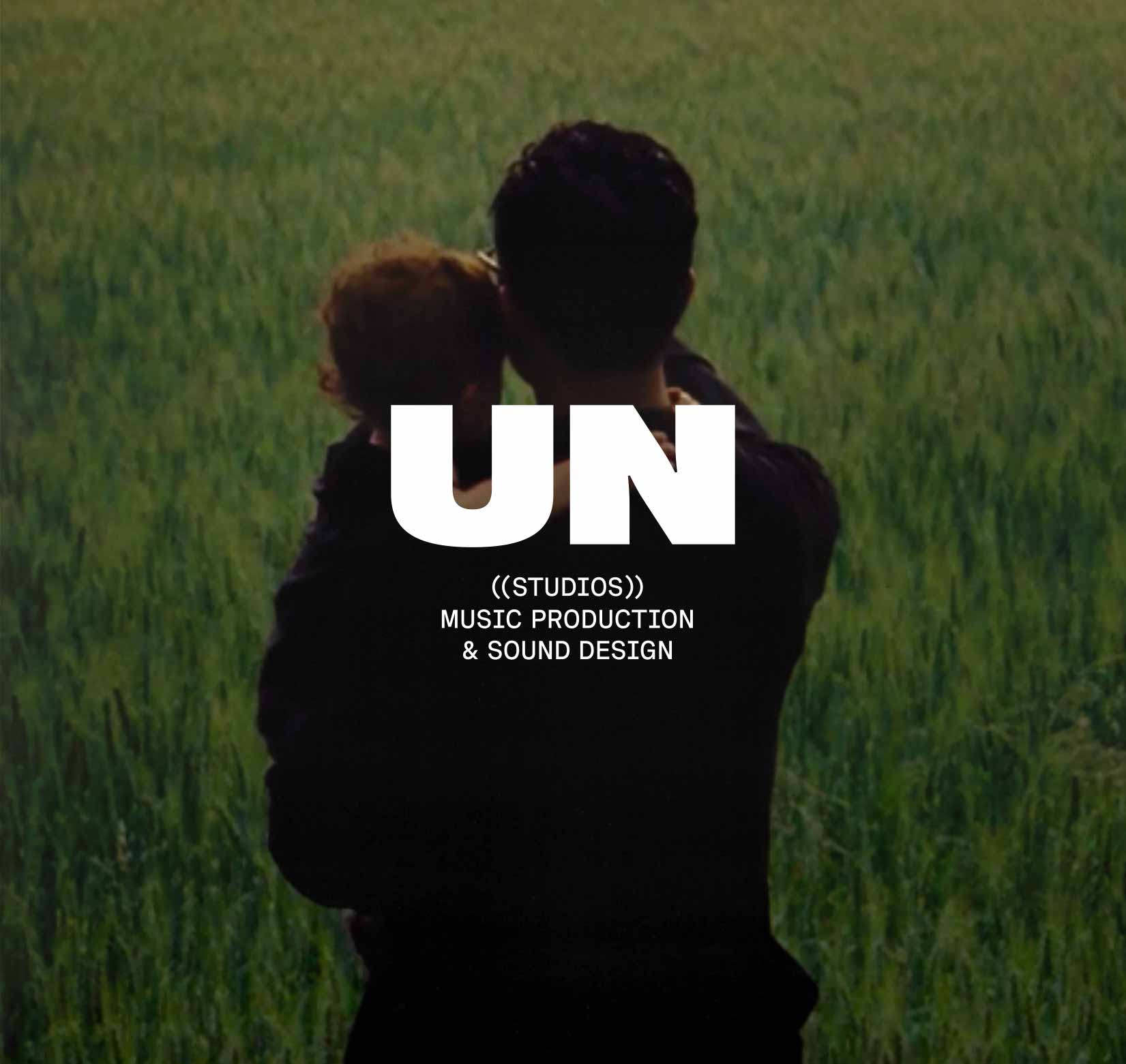 The image shows a man from the back holding a small child and pointing towards a field of grass with the unstudios logo in white over it.