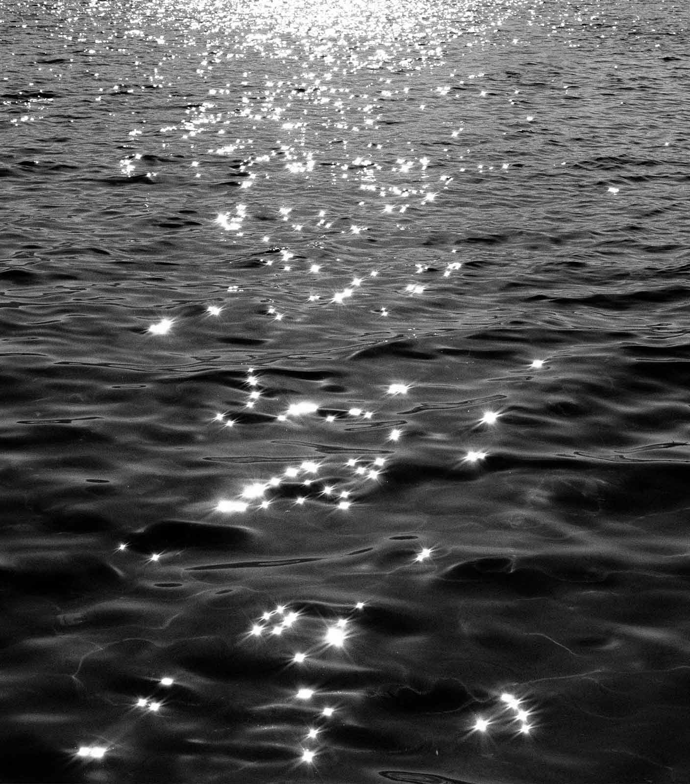A high contrast black-and-white photo of the ocean gently moving with sunshine reflecting from the water surface in beautiful sparkles.