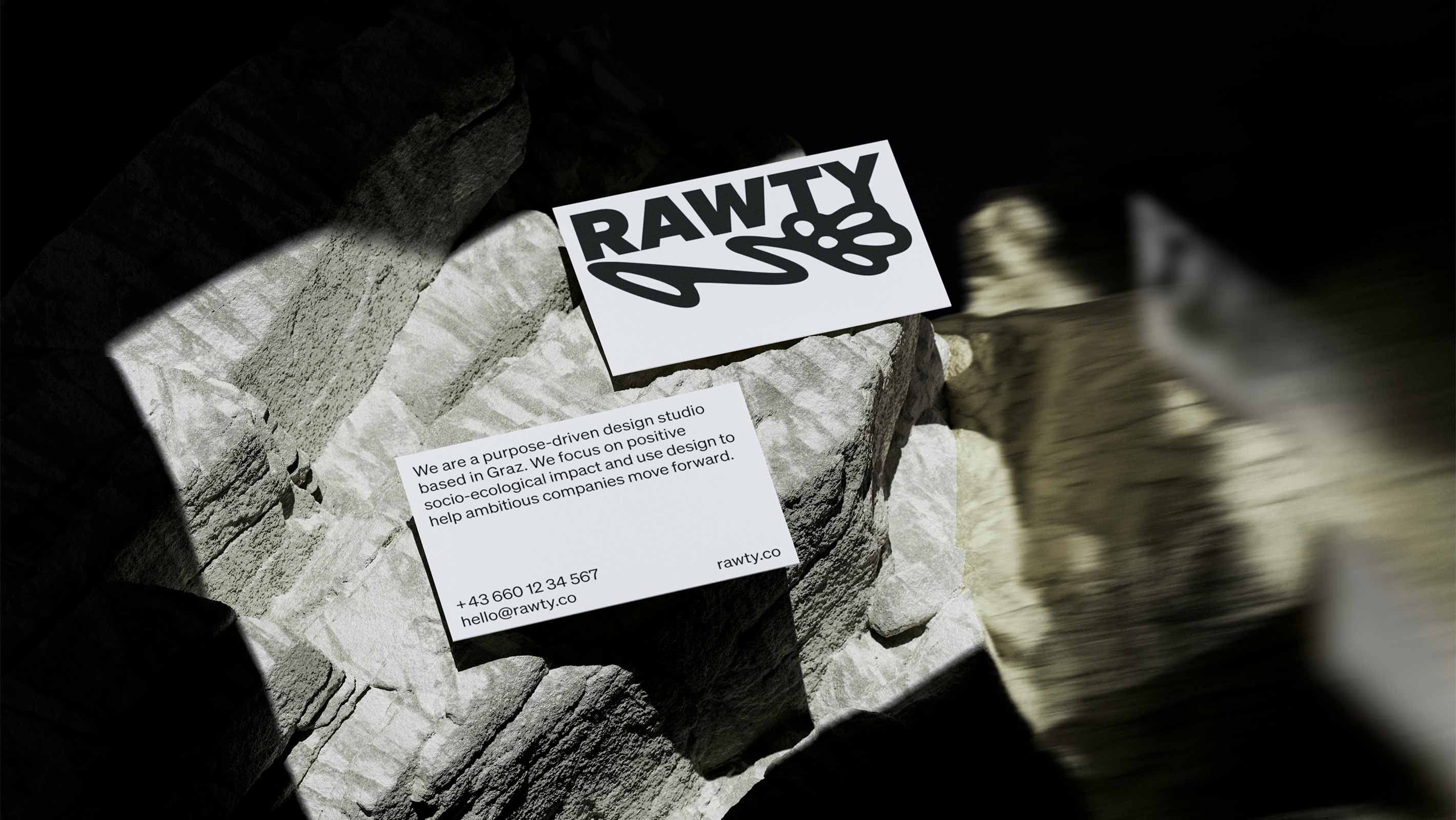 Business card of RAWTY on a stone in harsh sunlight and shadows with reflections on the right side.