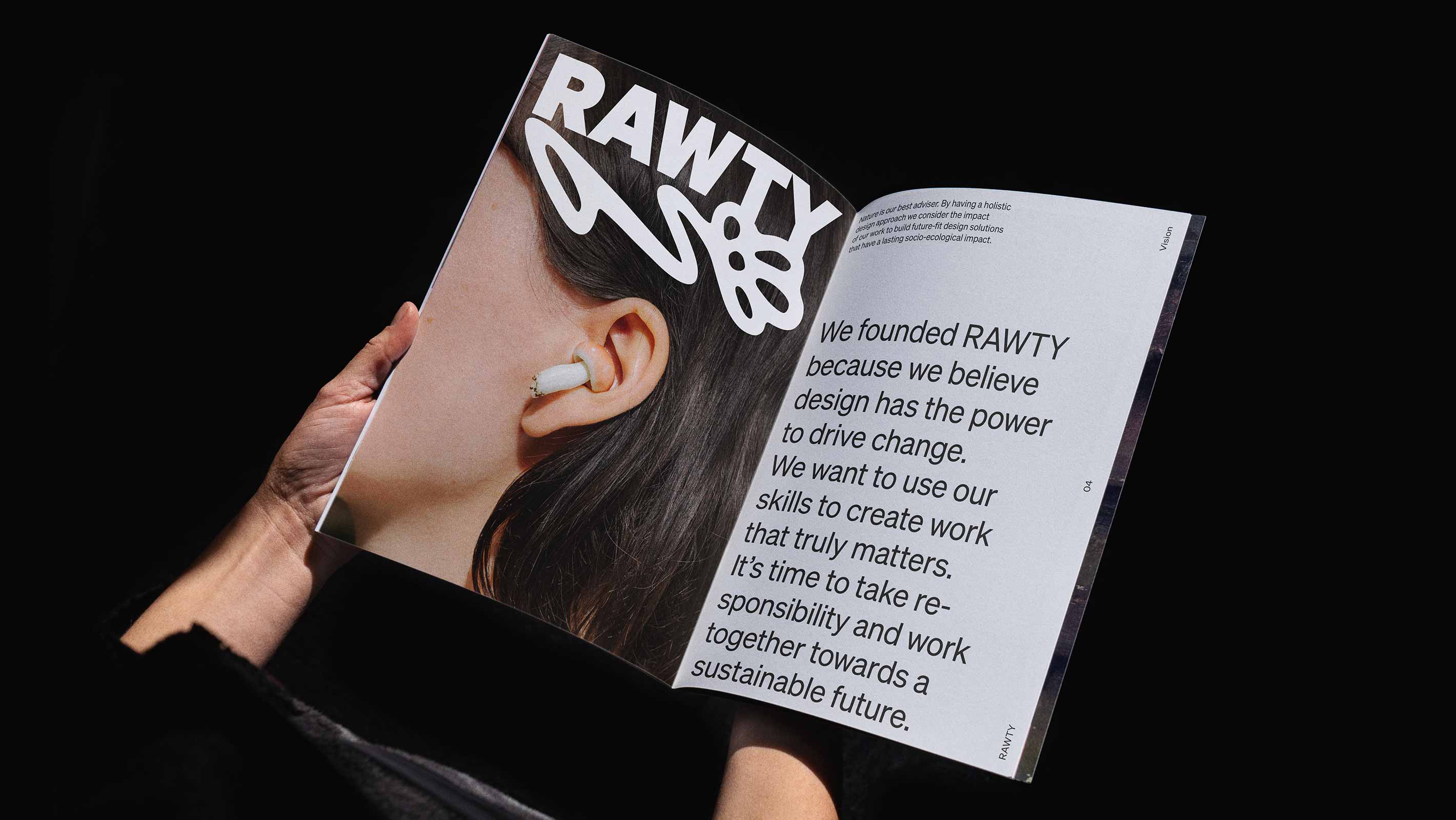 Two hands holding a magazine with an open spread where the left page shows a close-up photo of a woman with black hair and a small mushroom in her ear looking like a bluetooth headphone with the RAWTY logo over the photo at the top and the other side showing text about why we founded RAWTY.