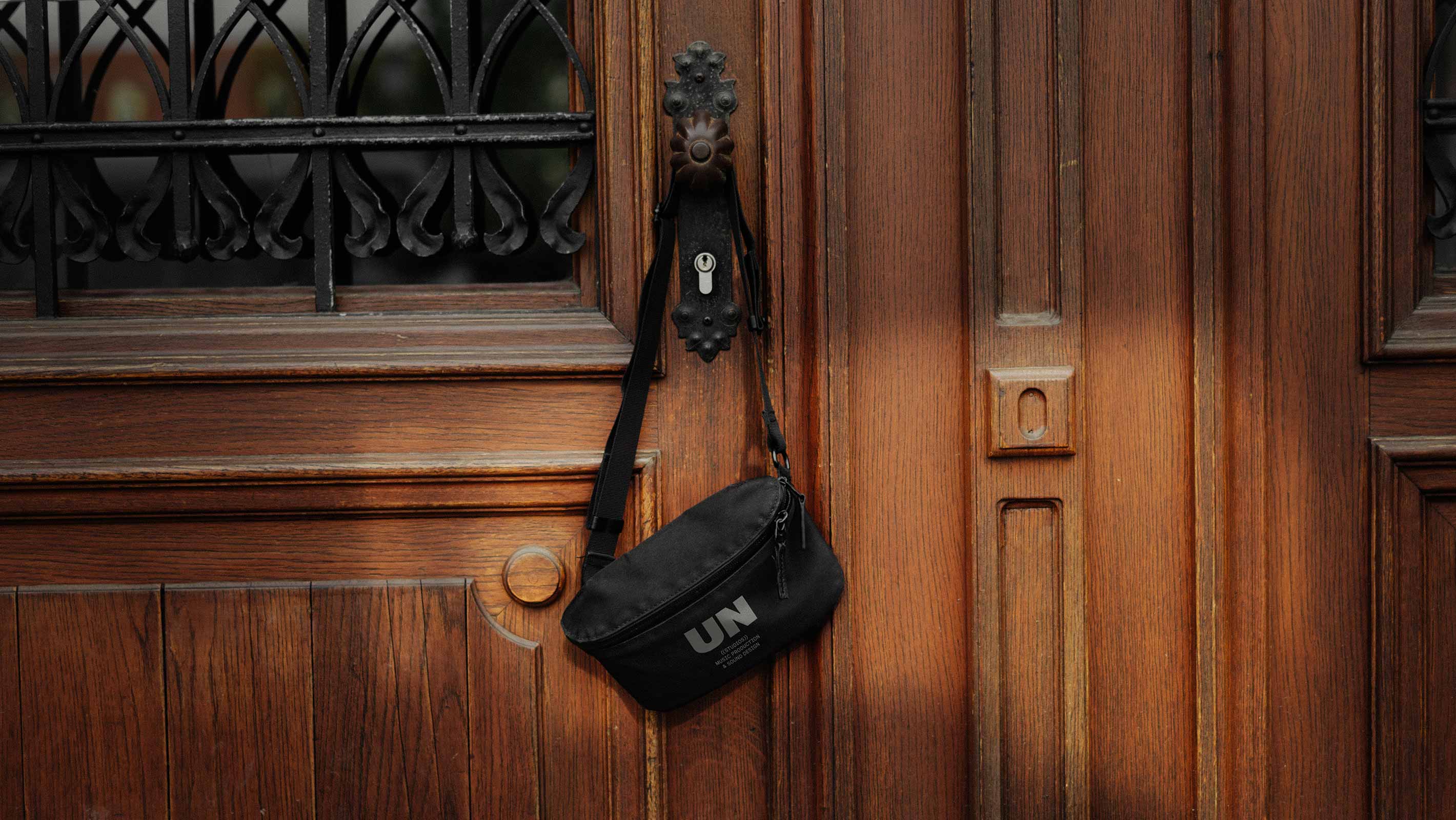 A fanny-bag with the unstudio-logo hanging on a doorknob of a beautiful old wooden door with natural light shining on the bag.